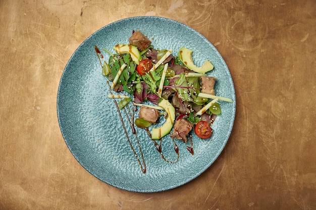 Salade met gegrilde tonijn, rucola, cherrytomaatjes, avocado en komkommer in een blauwe keramische plaat