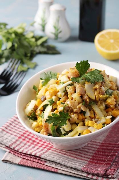 Salade met gerookte vis, maïsuien en mosterd in een witte kom op lichtblauwe achtergrond