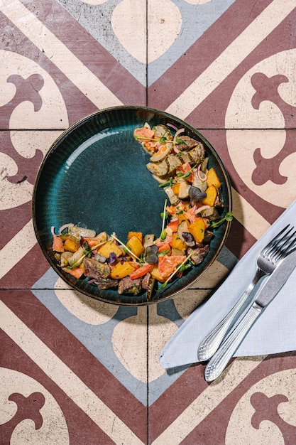 Salade met gestoofde kalfswangen, aardappelpartjes, tomaten en mosterdsaus vintage tegel achtergrond bovenaanzicht