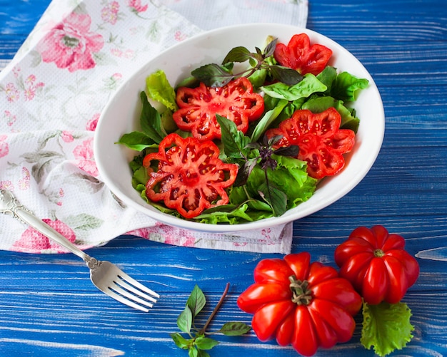 Foto salade met grote rijpe rode tomaat met basilicum op een blauwe houten tafel