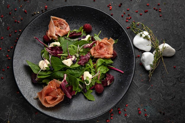 Salade met ham, kruiden, frambozen, microgreens op een donkere betonnen tafel