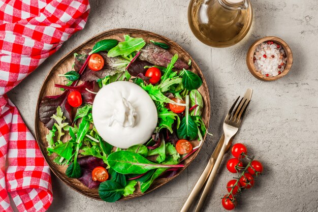 Salade met Italiaanse burrata kaas, rucola, spinazie, tomaten en olijfolie geserveerd op houten plaat