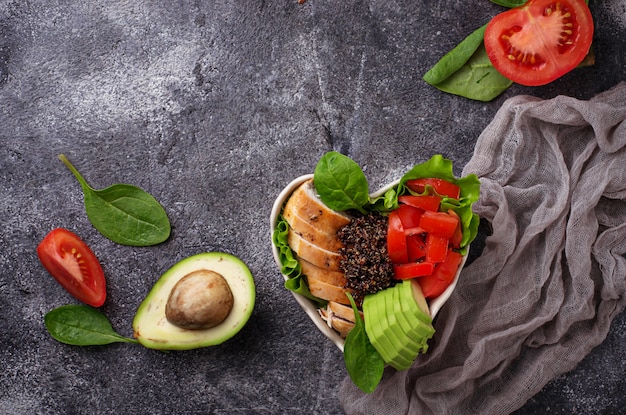 Salade met kip, zwarte quinoa, tomaten en avocado op de kom in de vorm van een hart. Gezonde balans