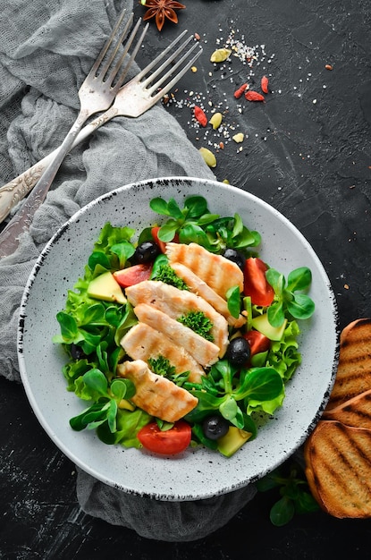 Salade met kipfilet, olijven, tomaten en avocado's in een bord op een houten achtergrond Bovenaanzicht Vrije ruimte voor uw tekst Plat leggen