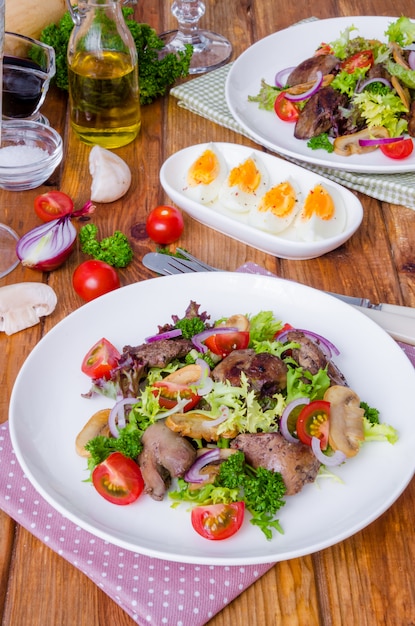 Salade met kippenlever, gebakken champignons en tomaten op een donker hout