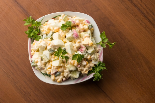 Salade met krabsticks, suikermaïs, komkommer, eieren en mayonaise op houten tafel. Bovenaanzicht