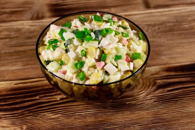 Salade met krabsticks, suikermaïs, komkommer, eieren, rijst en mayonaise op houten tafel