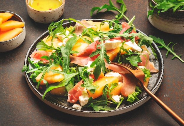 Salade met meloen jamon geitenkaas en rucola op bruine achtergrond bovenaanzicht kopie ruimte