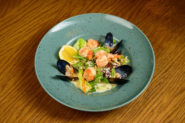 Salade met oesters, garnalen en groenten op blauw bord op houten achtergrond, bovenaanzicht