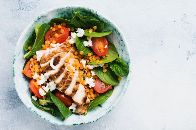 Salade met rode linzen, spinazieblaadjes, kerstomaatjes, kippenvlees en mozzarellakaas met olijfolie in keramische plaat