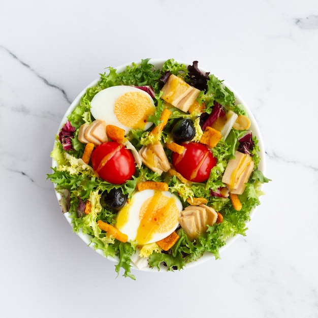 Foto salade met sla ei tonijn olijven en honing en mosterd vinaigrette op witte achtergrond