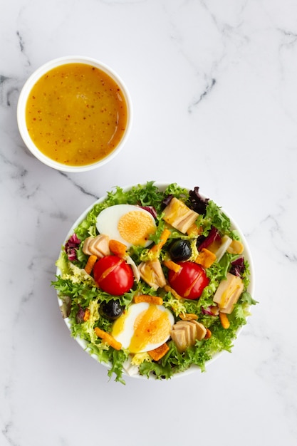 Foto salade met sla ei tonijn olijven en honing en mosterd vinaigrette op witte achtergrond