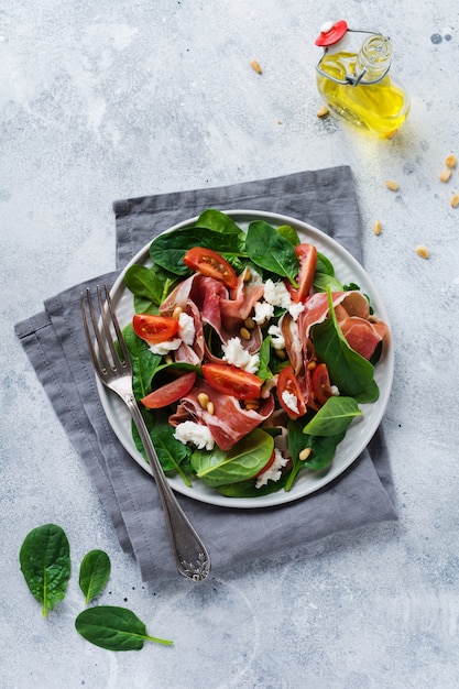 Salade met spinazie, cherrytomaat, mozzarella, pijnboompitten en ham met olijfolie op een oude betonnen grijze achtergrond.