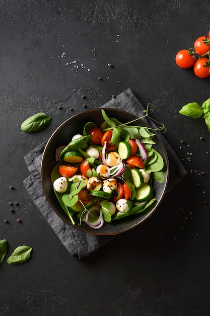 Foto salade met spinazie, zomergroenten en mozzarella op zwart. bovenaanzicht.