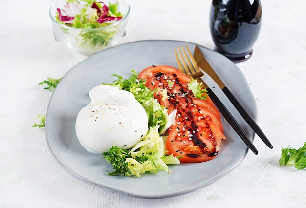 Salade met tomaten en burrata-kaas met sla en olijfolie op lichte Italiaanse keuken als achtergrond