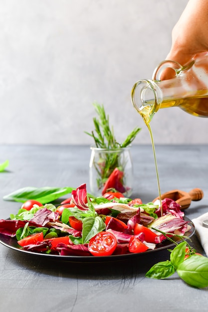 salade met tomaten en radicchio bladeren, basilicum met olijfolie en rozemarijn. olijfolie gieten