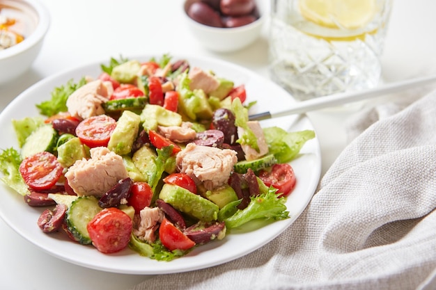 Salade met tonijnsla komkommers tomaten olijven en avocado's in witte plaat op tafel