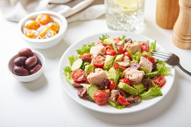 Salade met tonijnsla komkommers tomaten olijven en avocado's in witte plaat op tafel