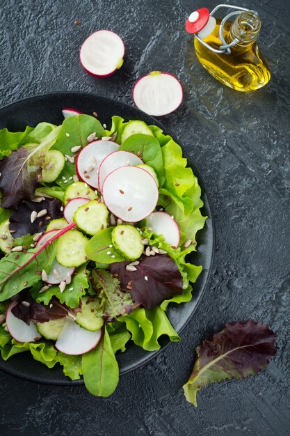 Salade met verse radijs, rucola, bieten, snijbiet, zonnebloempitten, lijnzaad en sesamzaadjes op een zwarte ondergrond