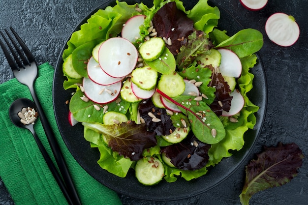 Salade met verse radijs, rucola, bieten, snijbiet, zonnebloempitten, lijnzaad en sesamzaadjes op een zwarte ondergrond