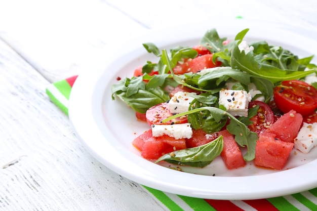 Salade met watermeloentomaten feta rucola en basilicumblaadjes op plaat op houten achtergrond