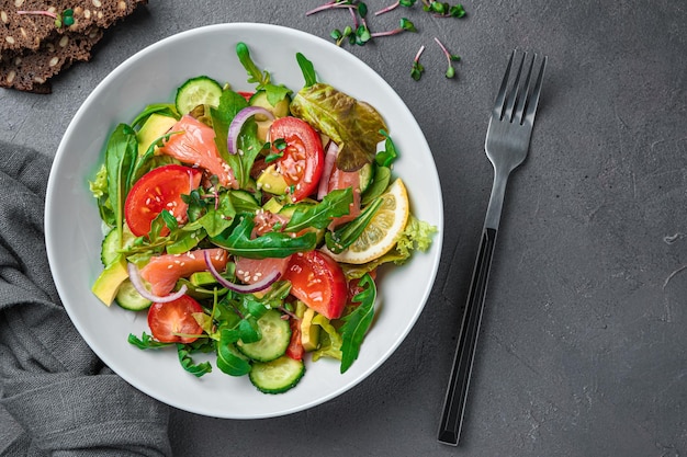 Salade met zalm, avocado, komkommer en tomaten op een donkergrijze achtergrond Gezonde voeding