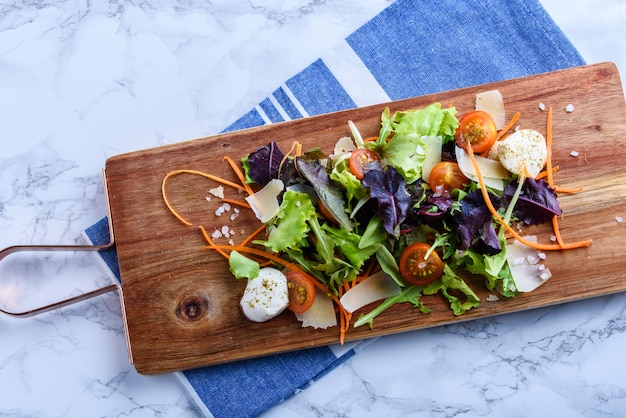 Salade op een houten bord met een servet en vork op marmeren diagonaal.