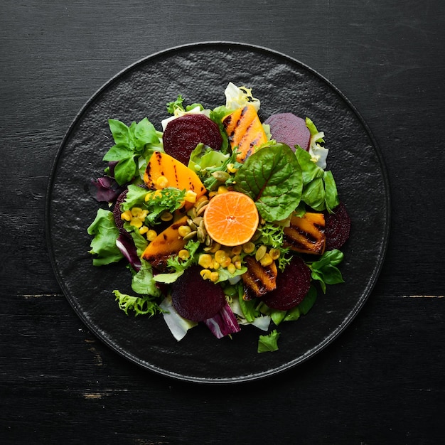 Salade rode biet pompoen maïs en sla in een zwarte plaat op een zwarte achtergrond Bovenaanzicht Vrije ruimte voor uw tekst