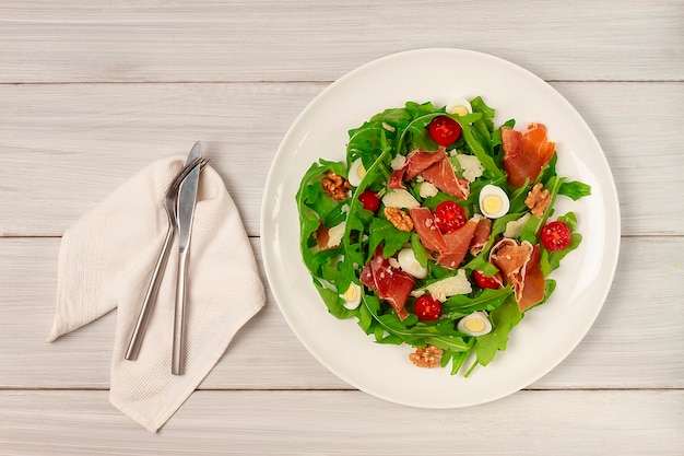 Salade, rucola bladeren met parma prosciutto kersen kwarteleitjes in een bord op houten achtergrond