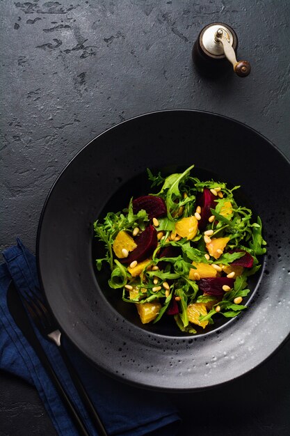 Salade van bieten, sinaasappel, pijnboompitten en rucola in zwarte keramische plaat op donkere betonnen tafeloppervlak. Bovenaanzicht.