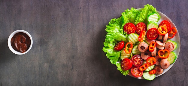 Salade van gebakken worstjes, tomaten, komkommer en sla op een webbanner met bovenaanzicht