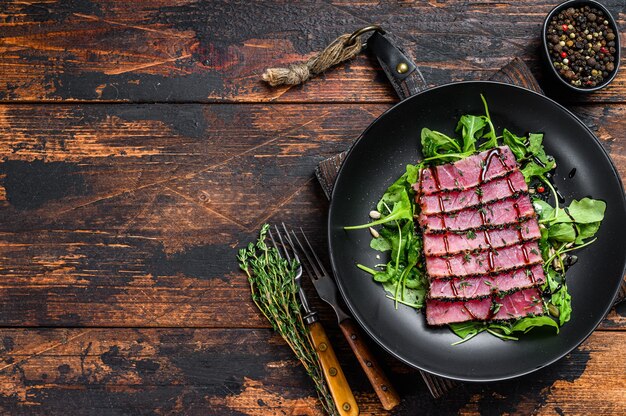 Salade van gegrilde teriyaki tonijnsteak met rucola en spinazie. Donkere houten achtergrond. Bovenaanzicht. Ruimte kopiëren.