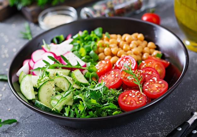 Salade van kikkererwten, tomaten, komkommers, radijs en greens. Dieet voedsel. Boeddha schaal. Veganistische salade.