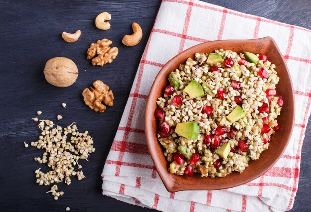 Salade van ontkiemde boekweit avocado walnoot en granaatappel zaden in kleiplaat op zwarte houten achtergrond