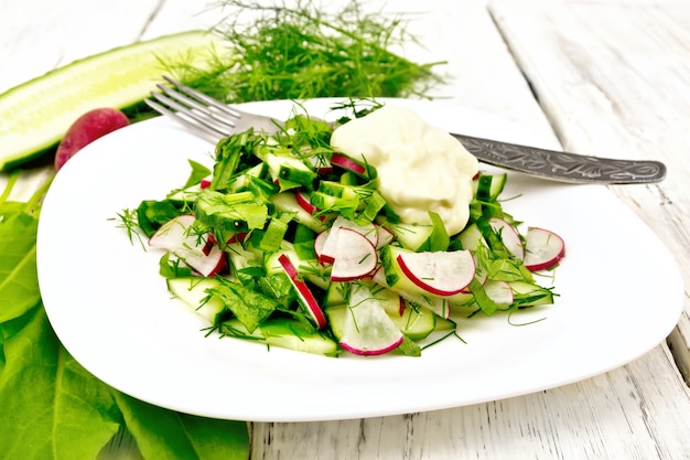 Salade van radijs, komkommer, zuring en greens, gekleed met mayonaise in een witte plaat op de achtergrond van houten plank