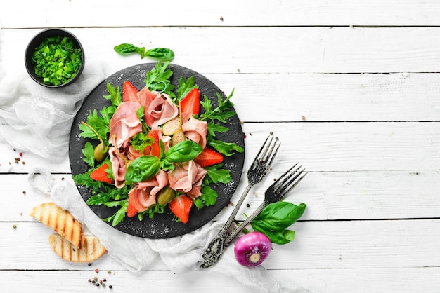 Salade van rucola prosciutto aardbeien en kappertjes op een zwarte stenen plaat Italiaanse keuken