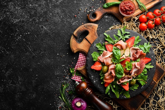 Salade van rucola prosciutto aardbeien en kappertjes op een zwarte stenen plaat Italiaanse keuken