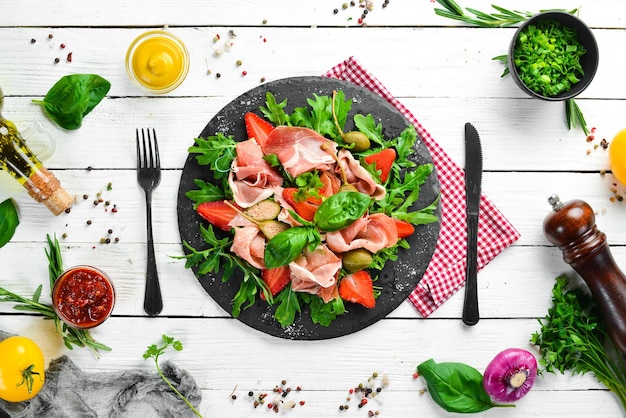 Salade van rucola prosciutto aardbeien en kappertjes op een zwarte stenen plaat Italiaanse keuken