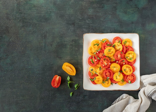 Salade van verse rode en gele tomaten met basilicum op een donkere achtergrond