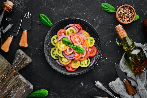 Salade van verse tomaten en ui in een zwarte plaat Op de oude achtergrond Bovenaanzicht Vrije ruimte voor uw tekst