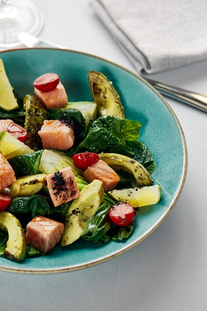 Salade van zalm en avocadofilet met artisjokken, gebakken zalmblokjes in saus met gegrilde groenten, avocado en artisjokken, lichte achtergrond, close-up.