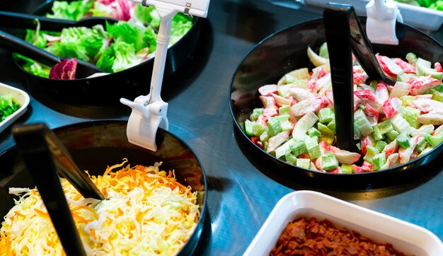 Saladebarbuffet in restaurant. Fris saladebuffet voor lunch of diner. Gezond eten. Selderij en krabstok die in zwarte kom op teller wordt gesneden. Horeca eten. Banket service. Vegetarisch eten.