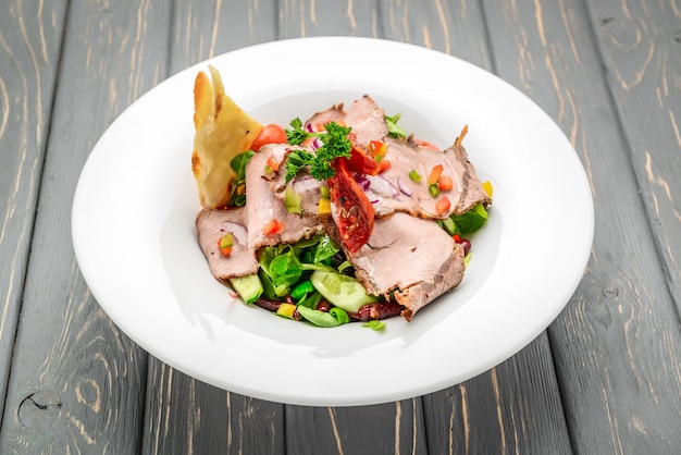 Saladebladeren met gesneden rosbief en in de zon gedroogde cherrytomaten