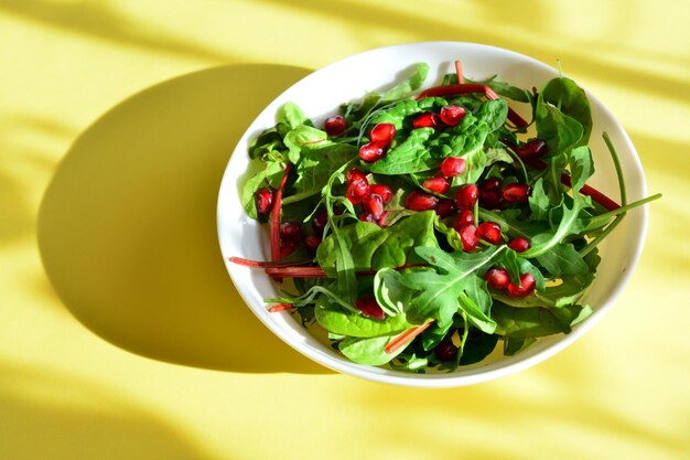 saladegroenten met granaatappelzaden in witte kom op de gele achtergrond met zonnestralen