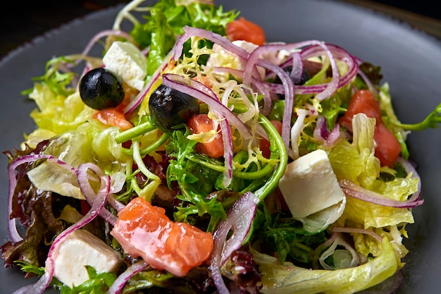 Salademix met zalm, fetakaas, uien en olijven, op een bord, op een houten ondergrond