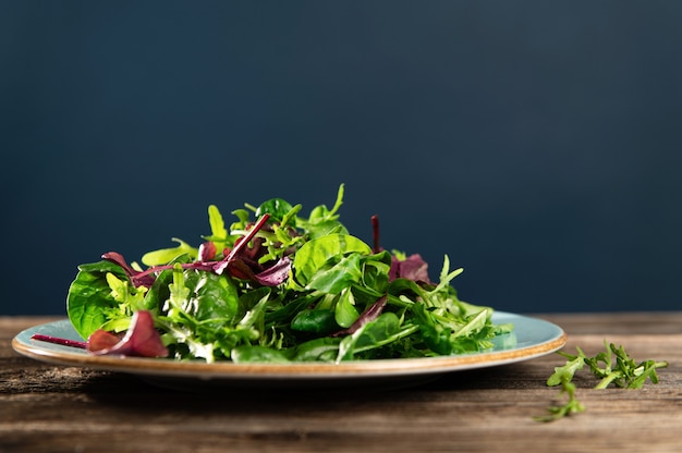 Salademix van verse kruiden, rucola, snijbiet en spinazie op een houten tafel en donkerblauwe achtergrond