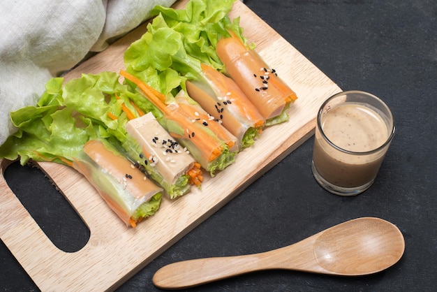 Saladerol op houten dienblad met saladedressing en houten lepel en linnen op houten zwarte tafel