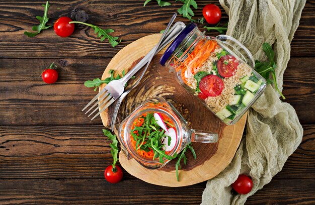 Salades met quinoa, rucola, radijs, tomaten en komkommer in glazen potten op houten tafel. Gezonde voeding, dieet, detox en vegetarisch concept. Bovenaanzicht Plat leggen