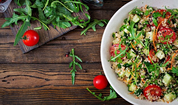 Salades met quinoa, rucola, radijs, tomaten en komkommer in kom op houten tafel. Gezonde voeding, dieet, detox en vegetarisch concept. Bovenaanzicht Plat leggen