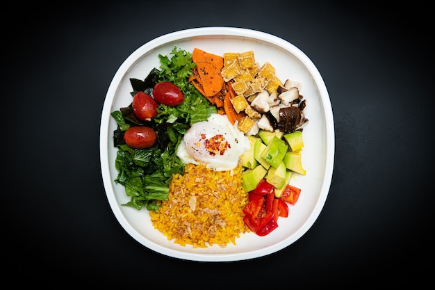 salads and various vegetables are on the white plate the background is black